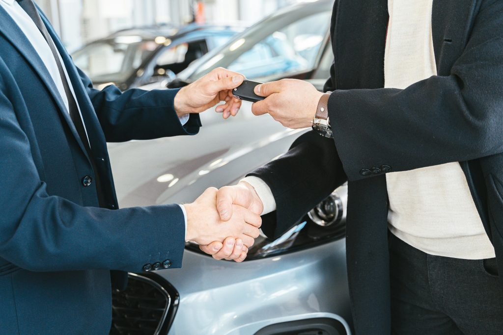 O nas Two businessmen shaking hands and exchanging car keys in a dealership. Symbolizes a successful deal.